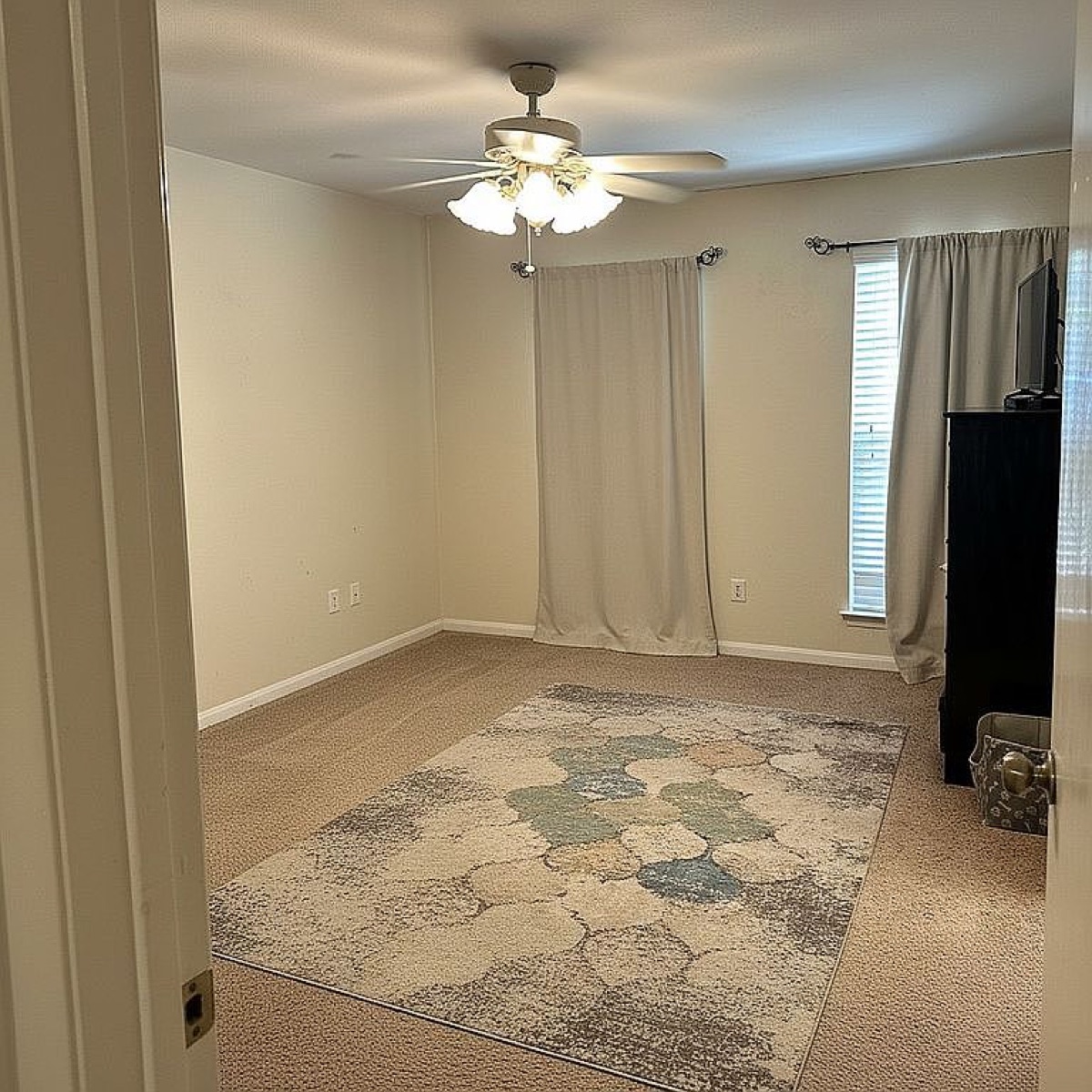 Original listing photo: an empty bedroom with beige carpet, a dresser and a rug, shot on a phone